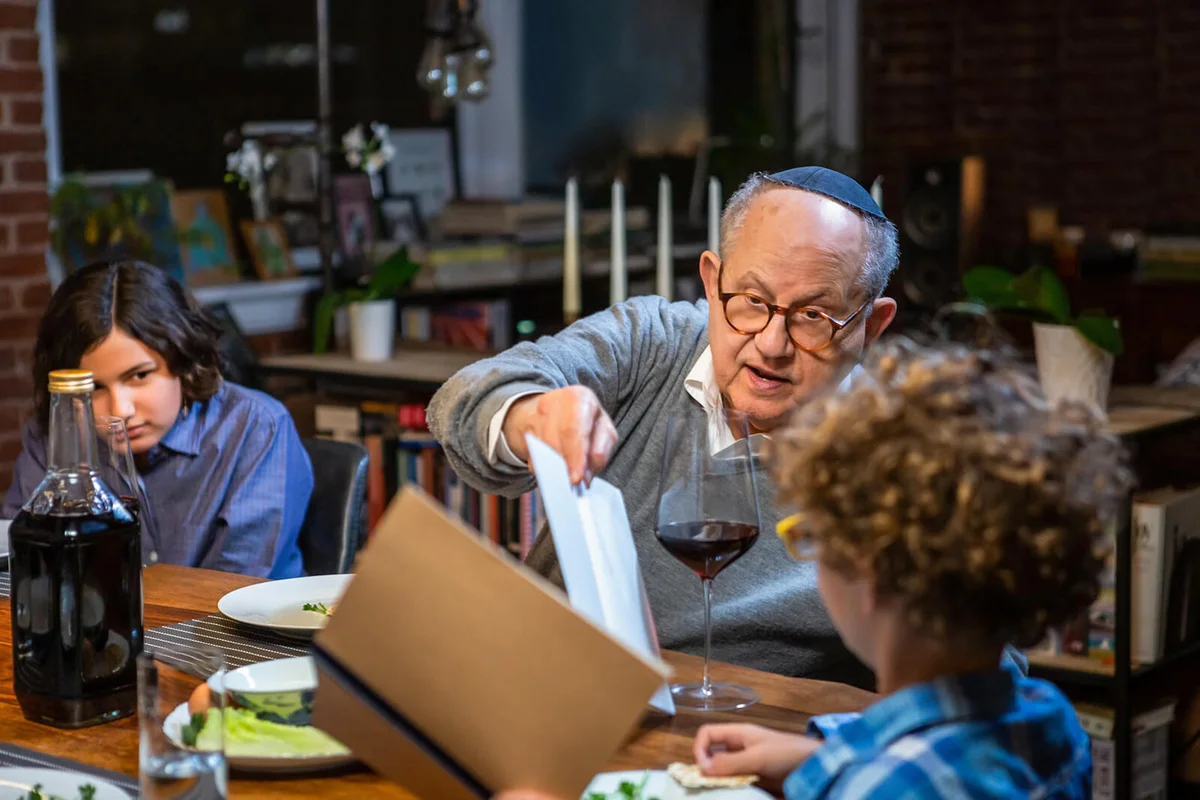Grandfather Helping Little Boy Read from Haggadah at Pasover Seder