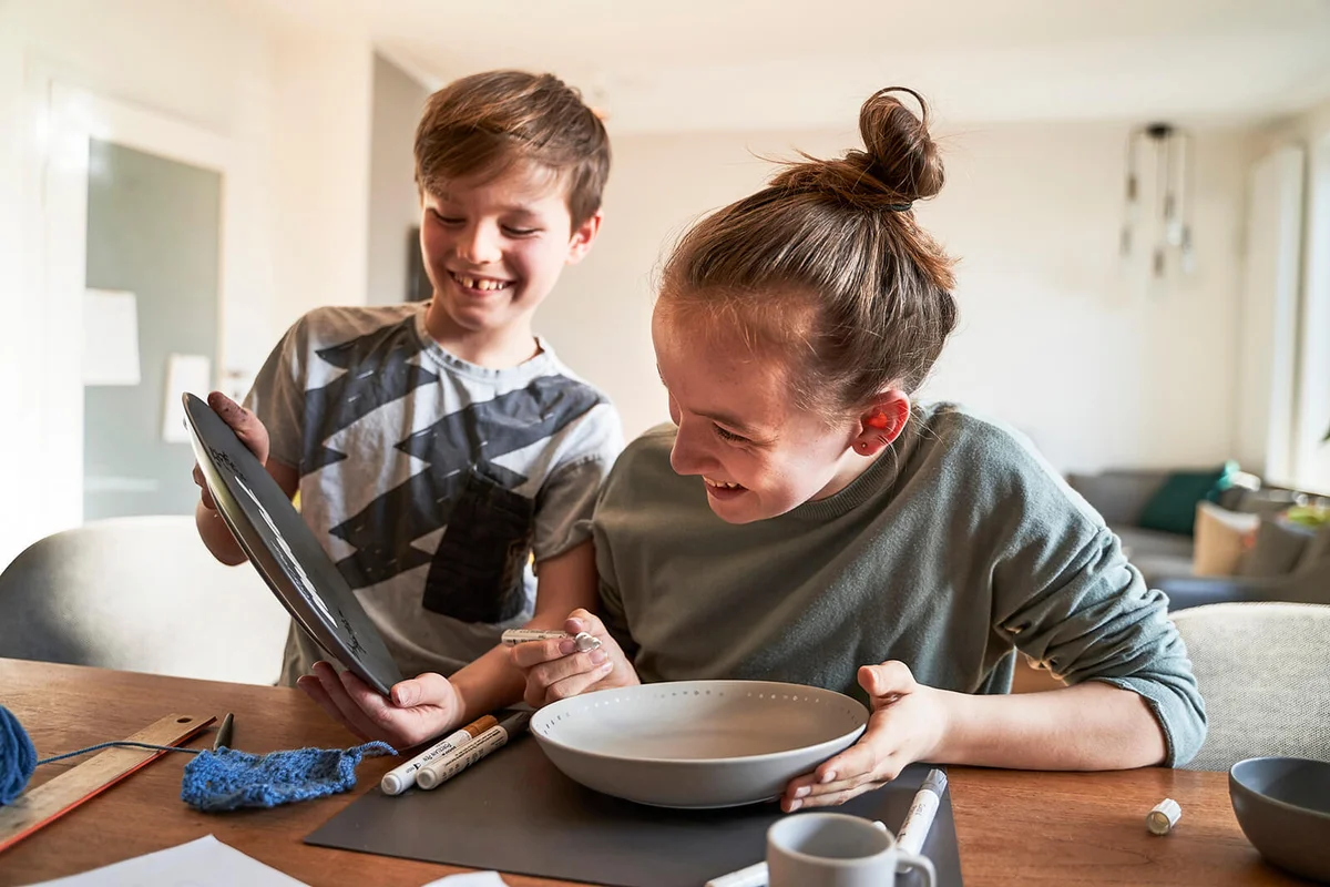 Happy brother and sister at home painting plate with porcelain paint