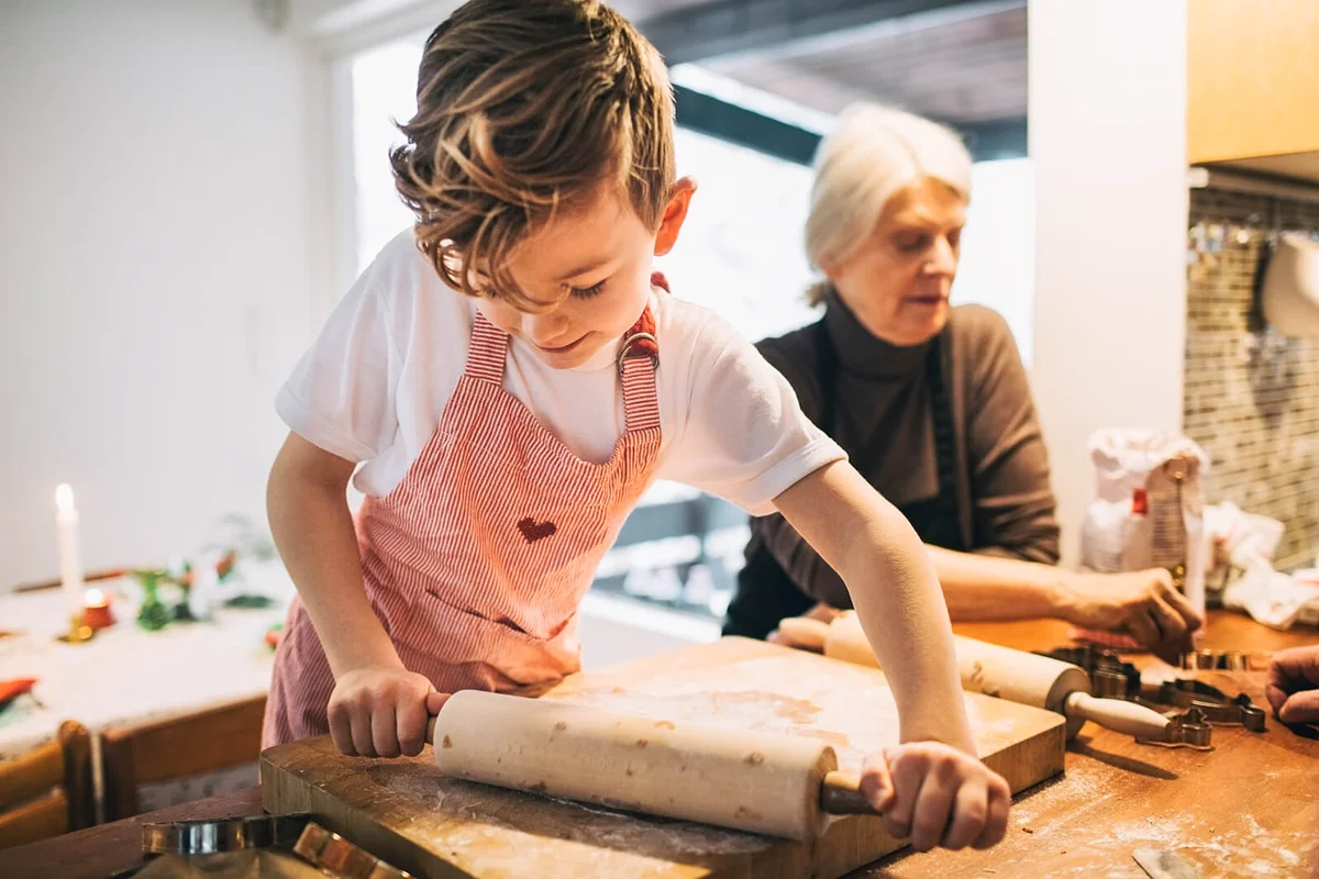 Boy rolling dough while standing by grandmother at kitchen counter