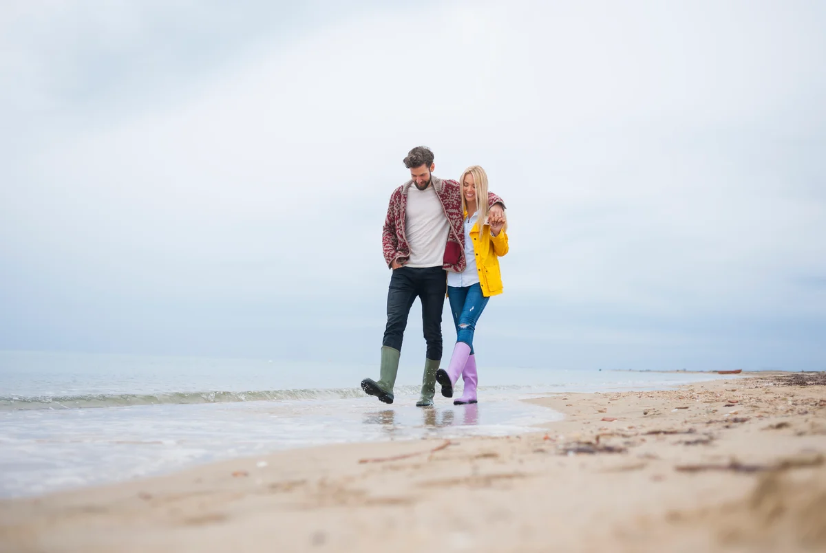 Couple in rain boots walking on beach in rainy weather