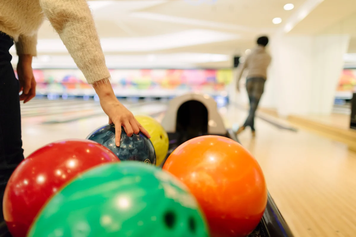 Person grabbing bowling ball at bowling alley