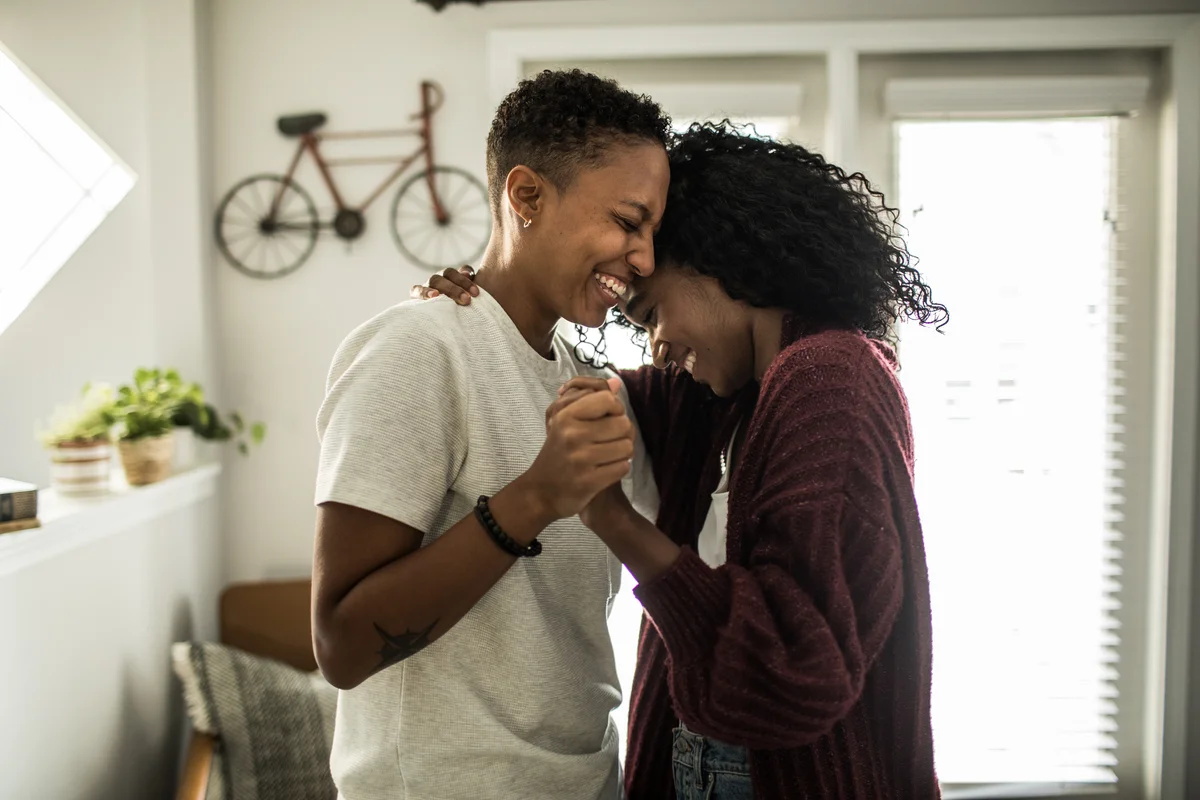 Young lesbian couple dancing and laughing in living room