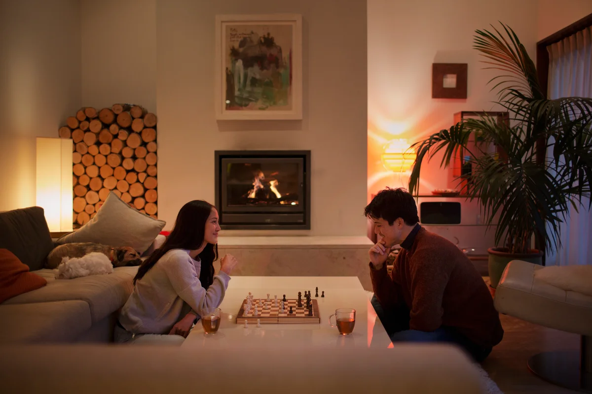 Couple playing chess in front of fireplace with mugs of tea