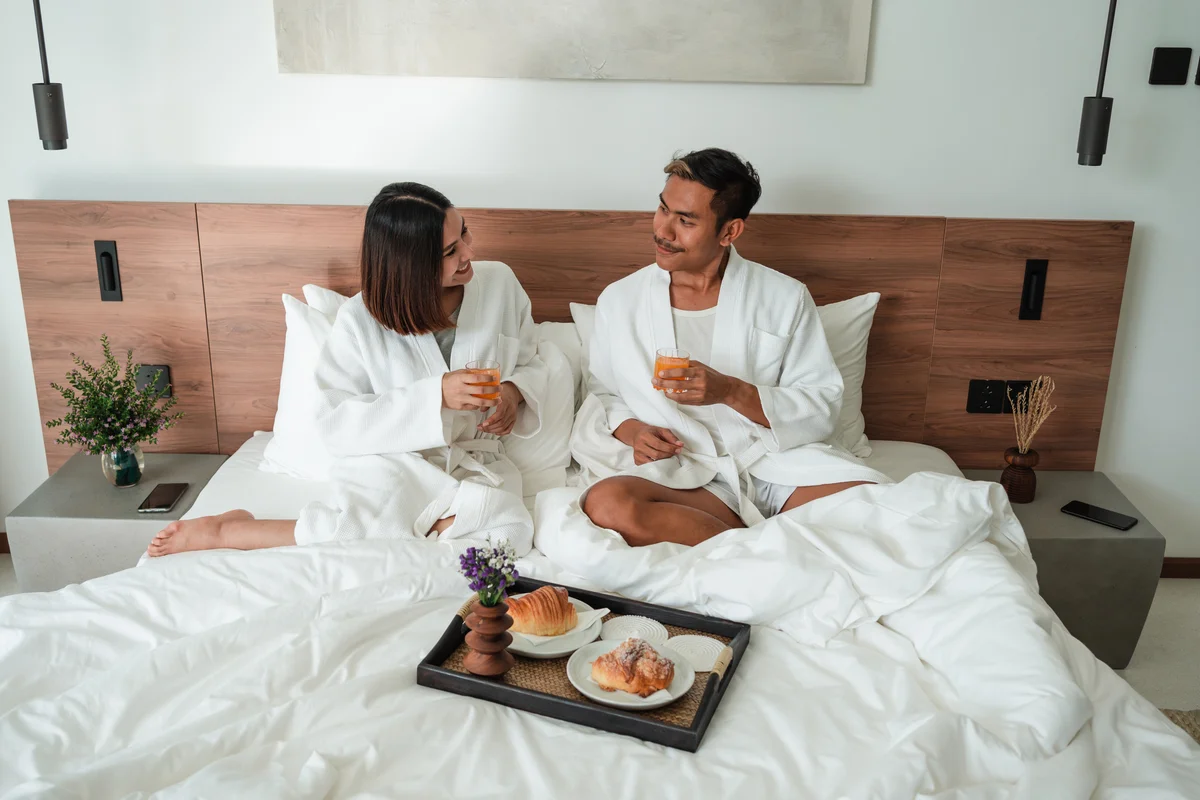 Couple in hotel room wearing white robes with room service food