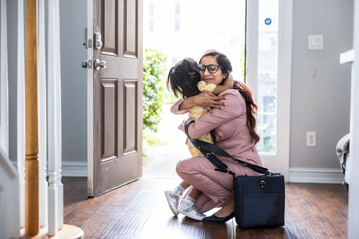 Toddler girl embracing mother in doorway