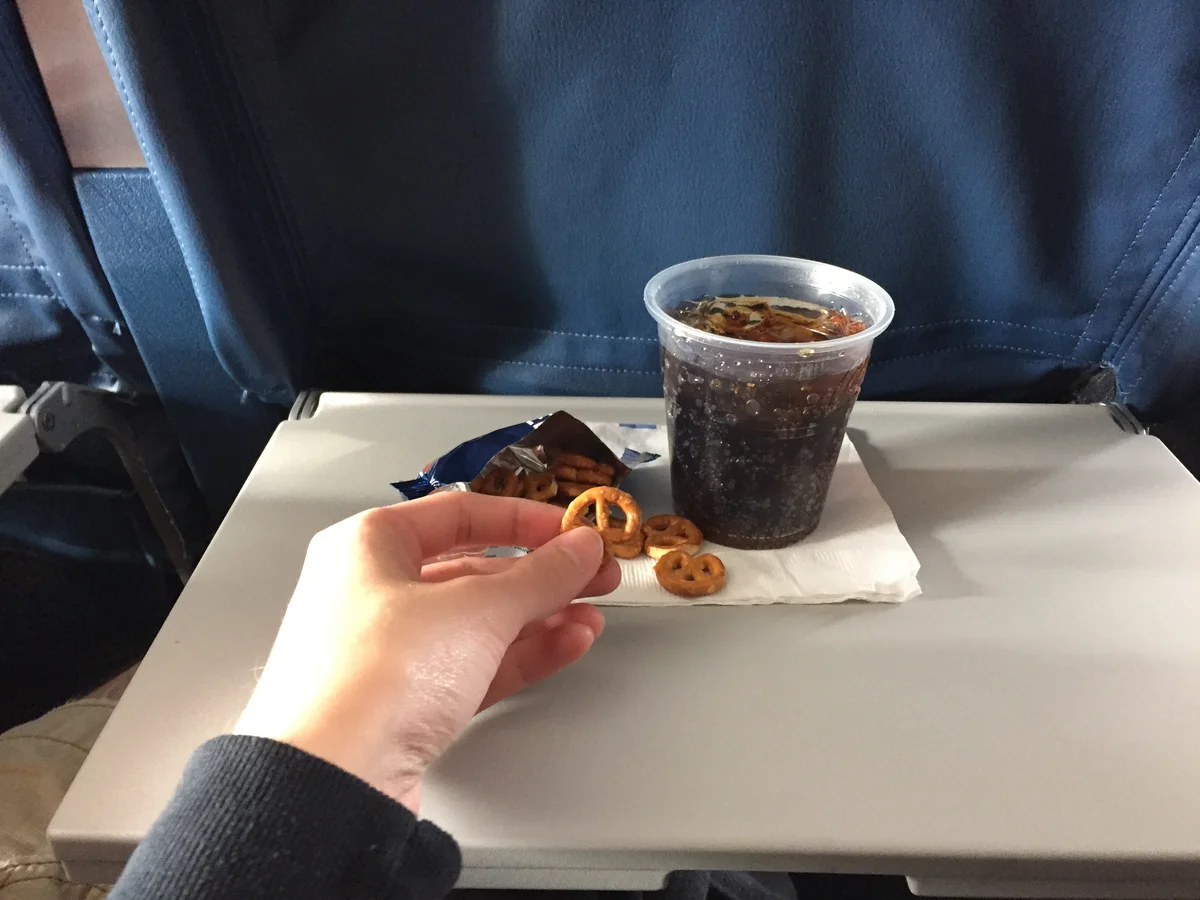 Person enjoying pretzels and soda on a plane