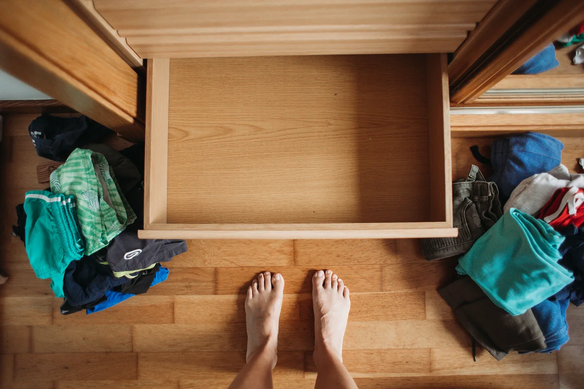 Empty dresser drawer and messy clothes all over the floor before organizing