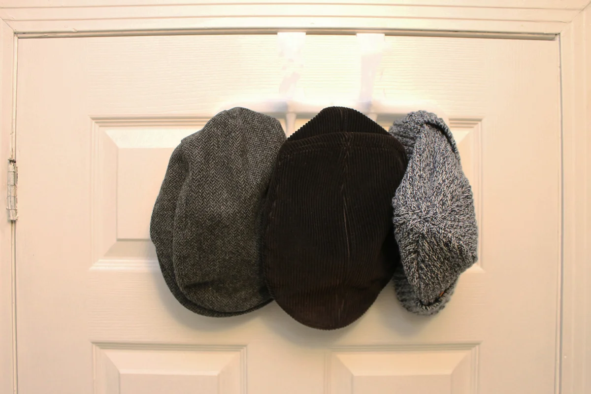Three gray hats hung on a hook on the back of a white door