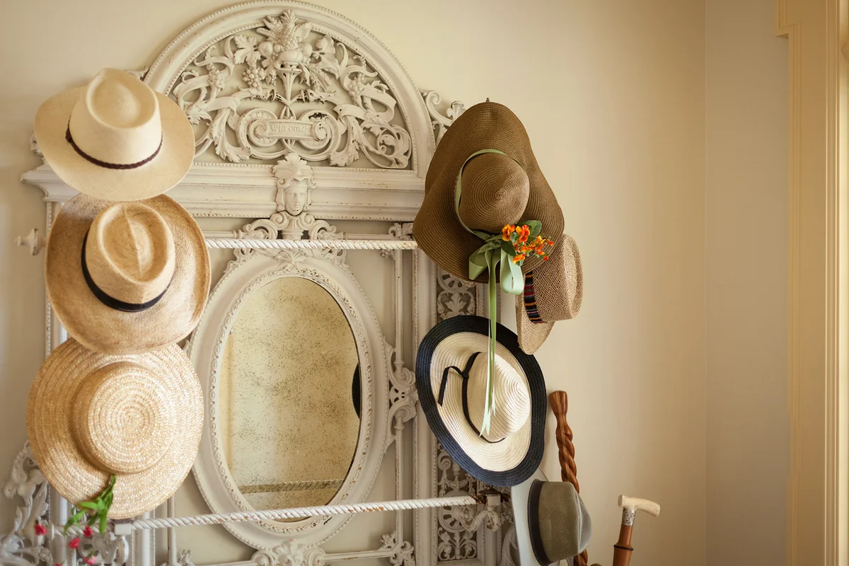 Collection of hats on an antique hat rack in home foyer interior with pale yellow walls