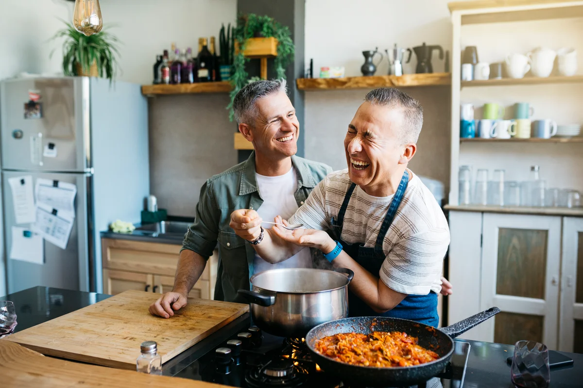 Happy middle-aged gay couple cooking in kitchen