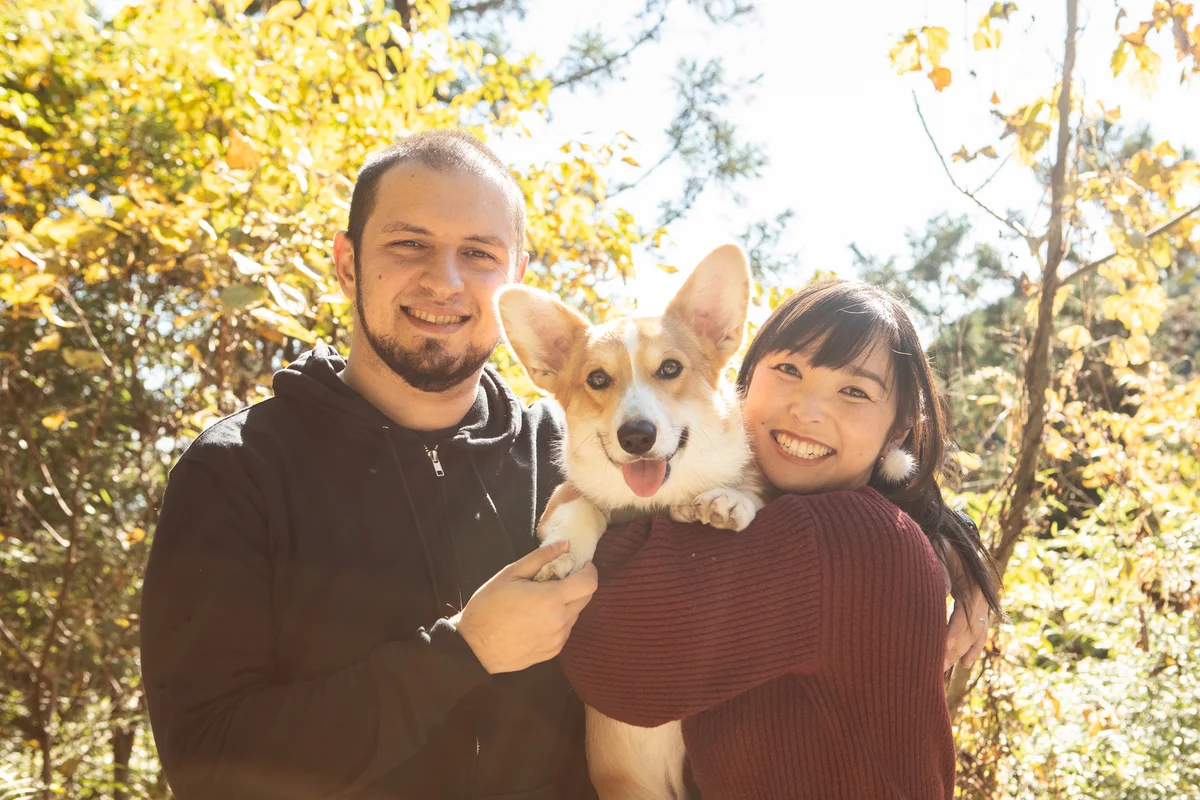 Couple in their thirties outside, smiling with their pet Corgi