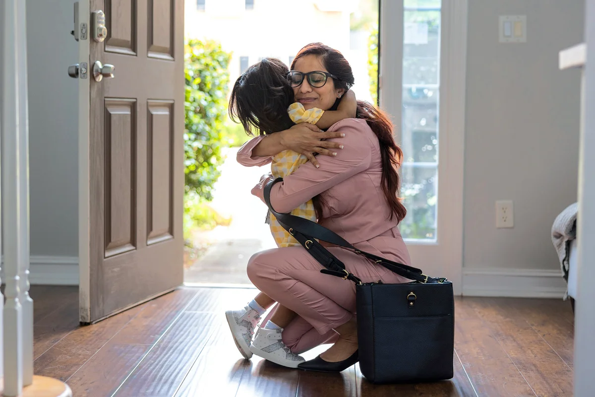 Toddler girl embracing mother in doorway as she gets home from work