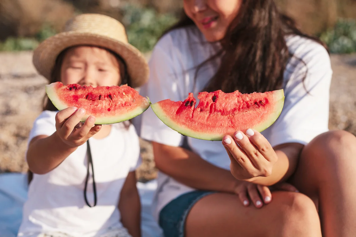 Mother and daughter eating watermelon and having fun at the beach