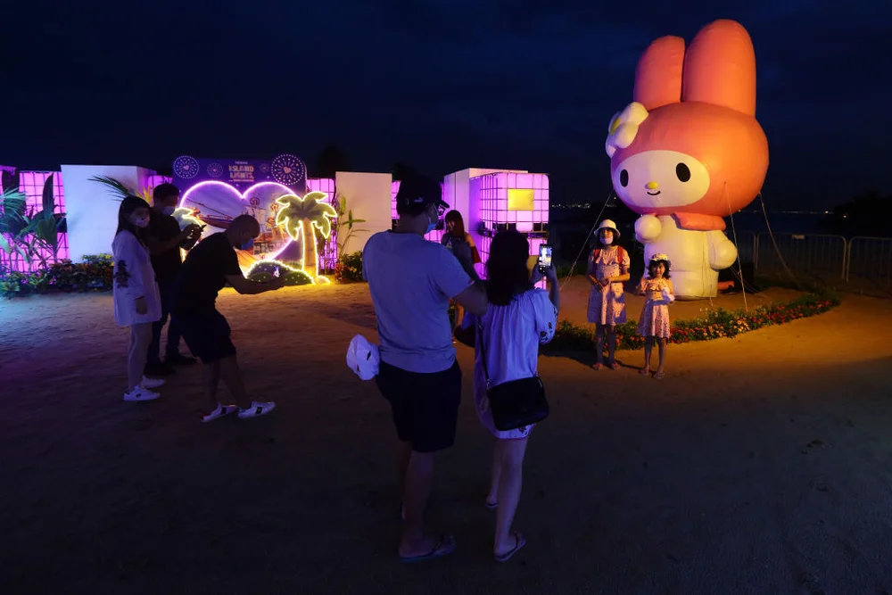 SINGAPORE - DECEMBER 16: People wearing protective mask takes a photo with a Sanrio character, My Melody during the Sentosa's festive light-up, Island Lights at Siloso beach, Sentosa on December 16, 2020 in Singapore. As of 16 December, the Ministry of Health confirmed 12 new imported COVID-19 cases with no cases in the wider community bringing the country's total to 58,353. (Photo by Suhaimi Abdullah/Getty Images)