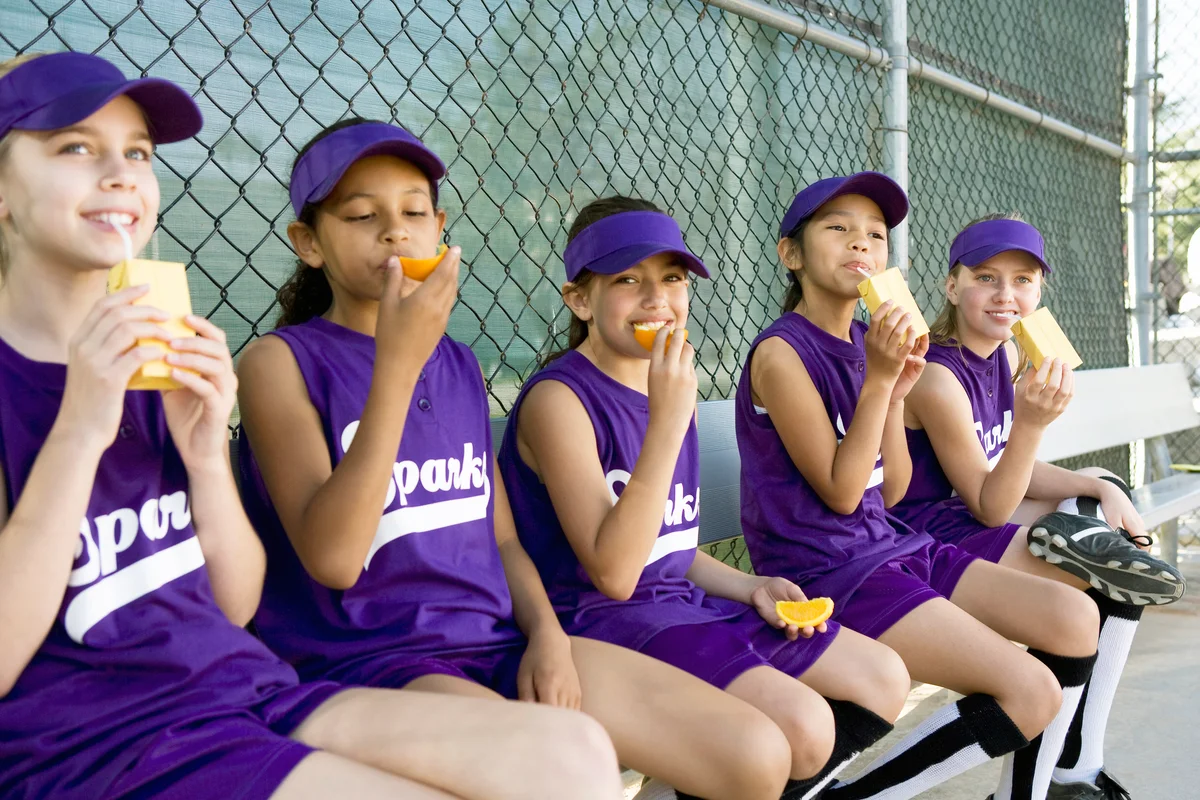 Little league players drinking juice boxes and eating orange