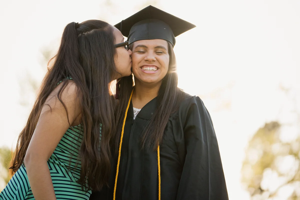 Girl kissing sister on cheek at graduation