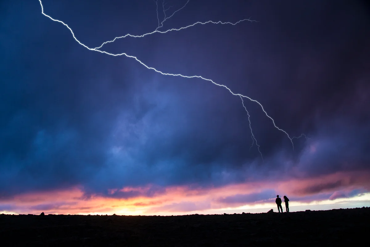Two hikers out in the open while lightning strikes