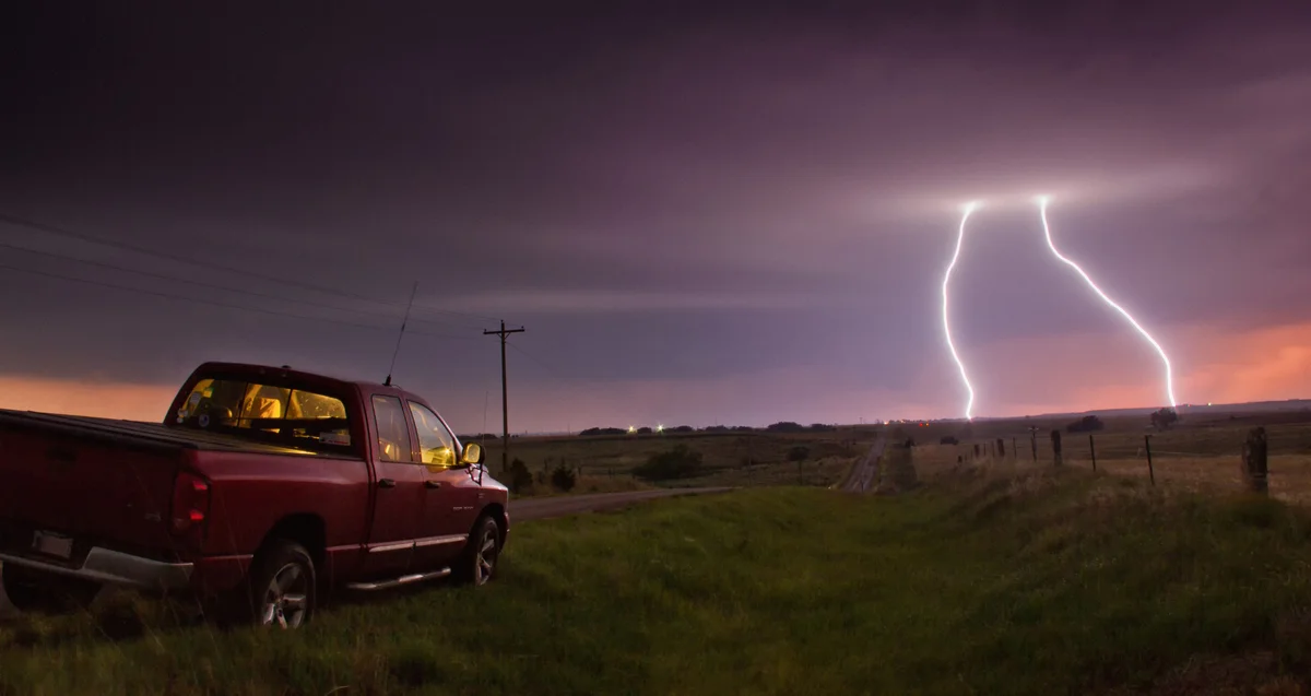 Truck pulled over on road while lightning strikes in distance