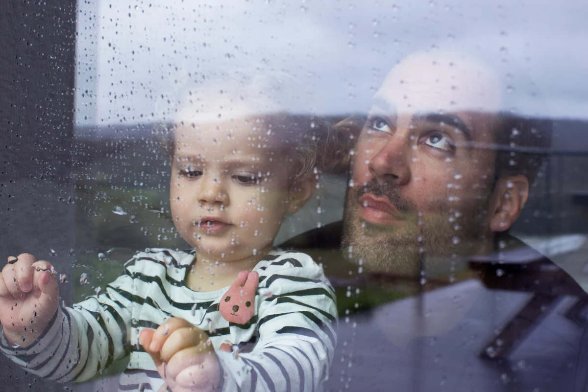 Dad and daughter watch rain storm from inside