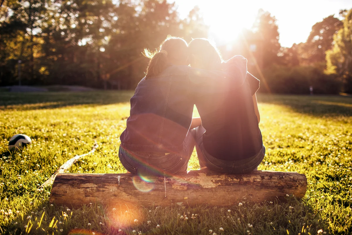 Silhouette of women sitting on log and hugging