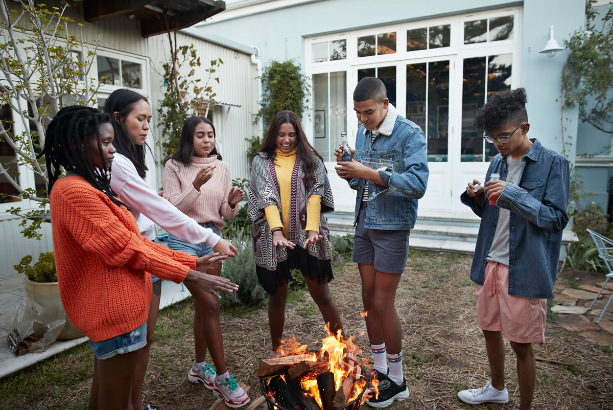 Male and female friends warming hands over bonfire in back yard