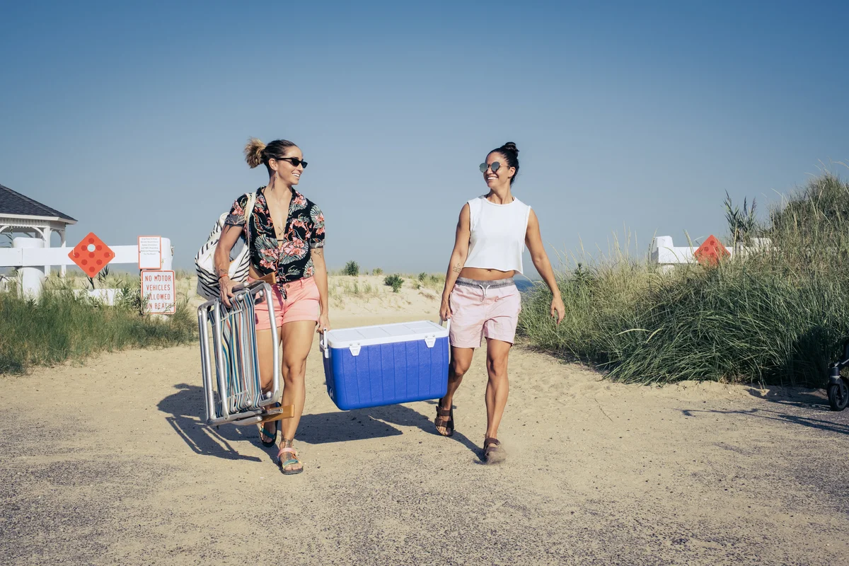 Lesbian couple carrying cooler onto New Jersey beach