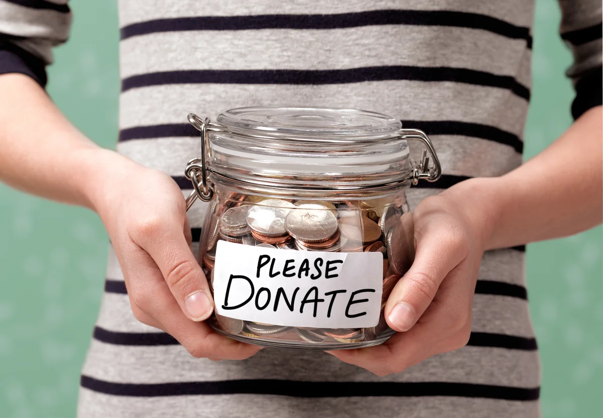 Woman holding jar of coins that says "please donate"