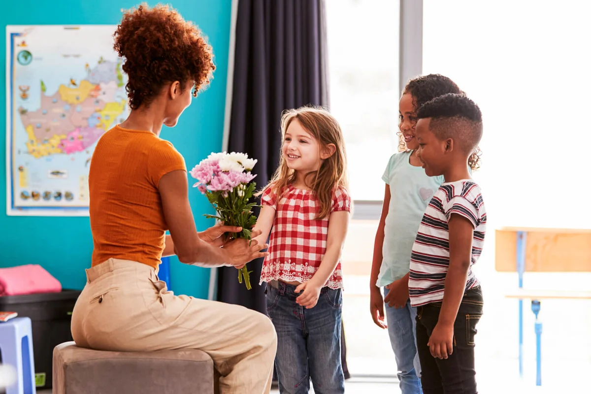 Group Of Elementary School Pupils Giving Female Teacher Thank You Gift Of Flowers