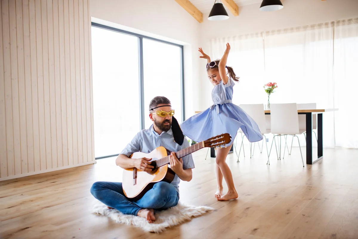 father and small daughter with guitar indoors at home, having fun