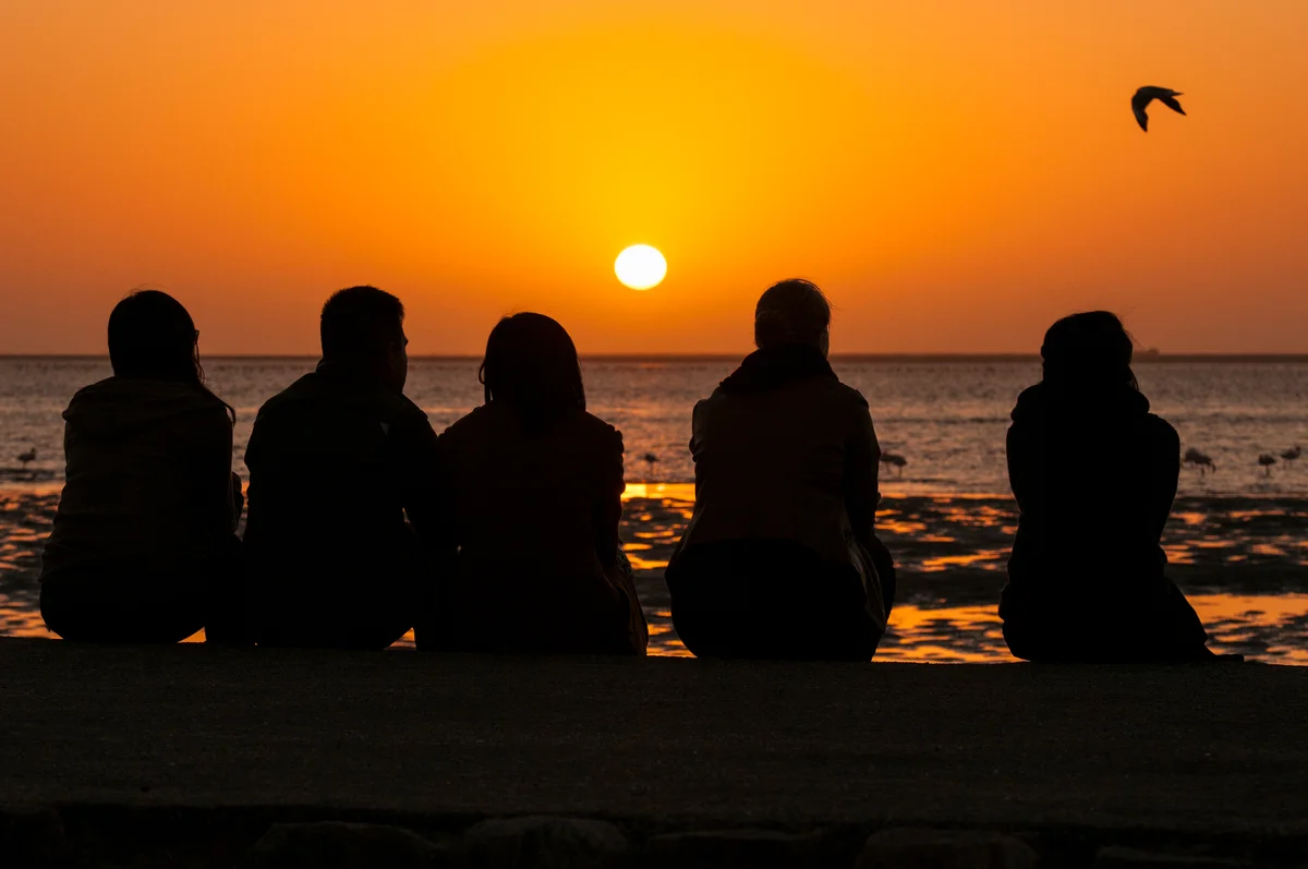 Silhouette of family sitting on beach watching sunset