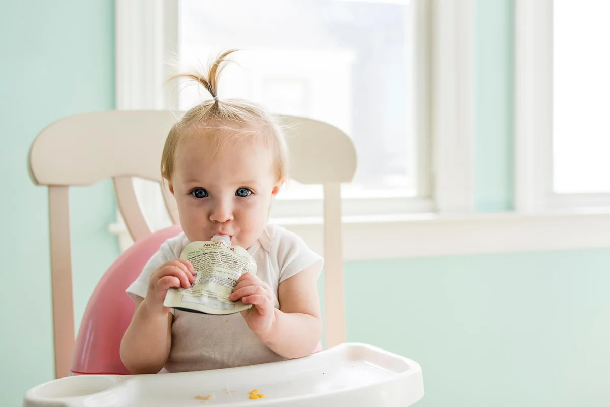 Portrait of cute baby girl eating apple sauce from pack