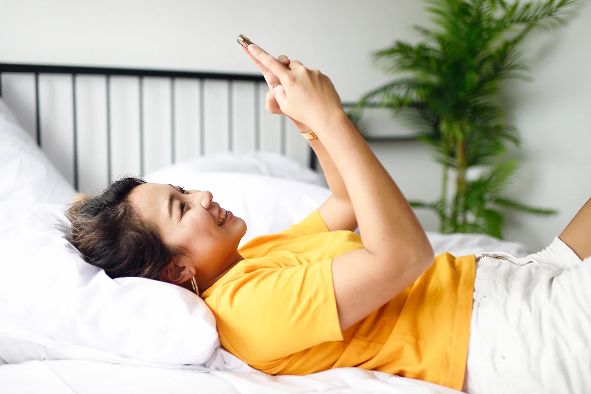 Young Malaysian woman reading from her phone in bed