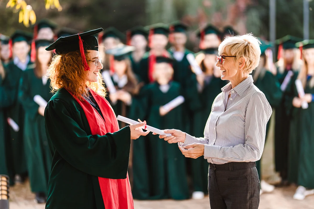 Happy senior professor giving diploma to female student on graduation day