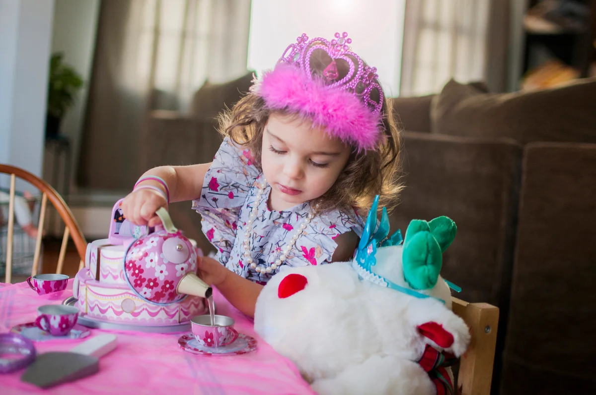 Little girl at her princess party serving tea to her stuffed animal