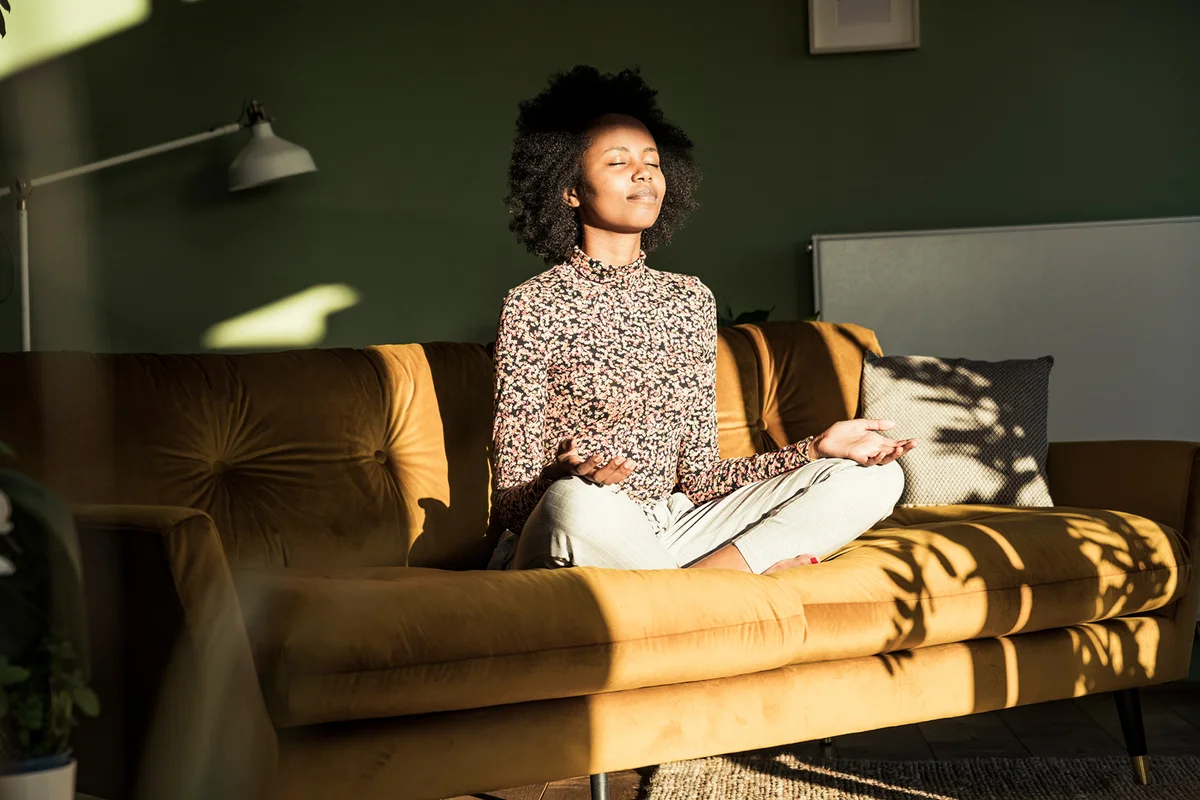 Woman meditating while sitting on sofa at home
