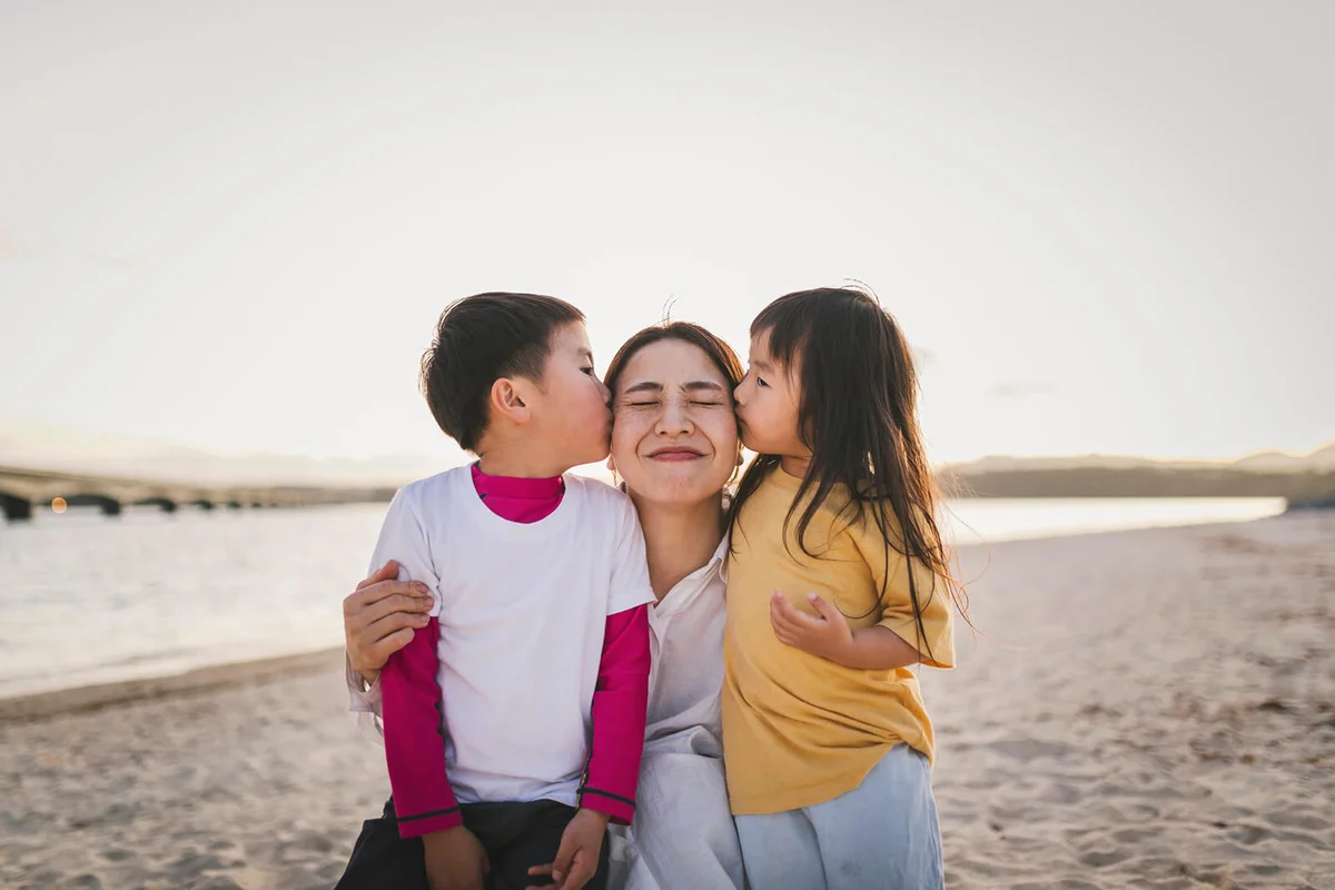 Kids kissing mother in the beach at dusk