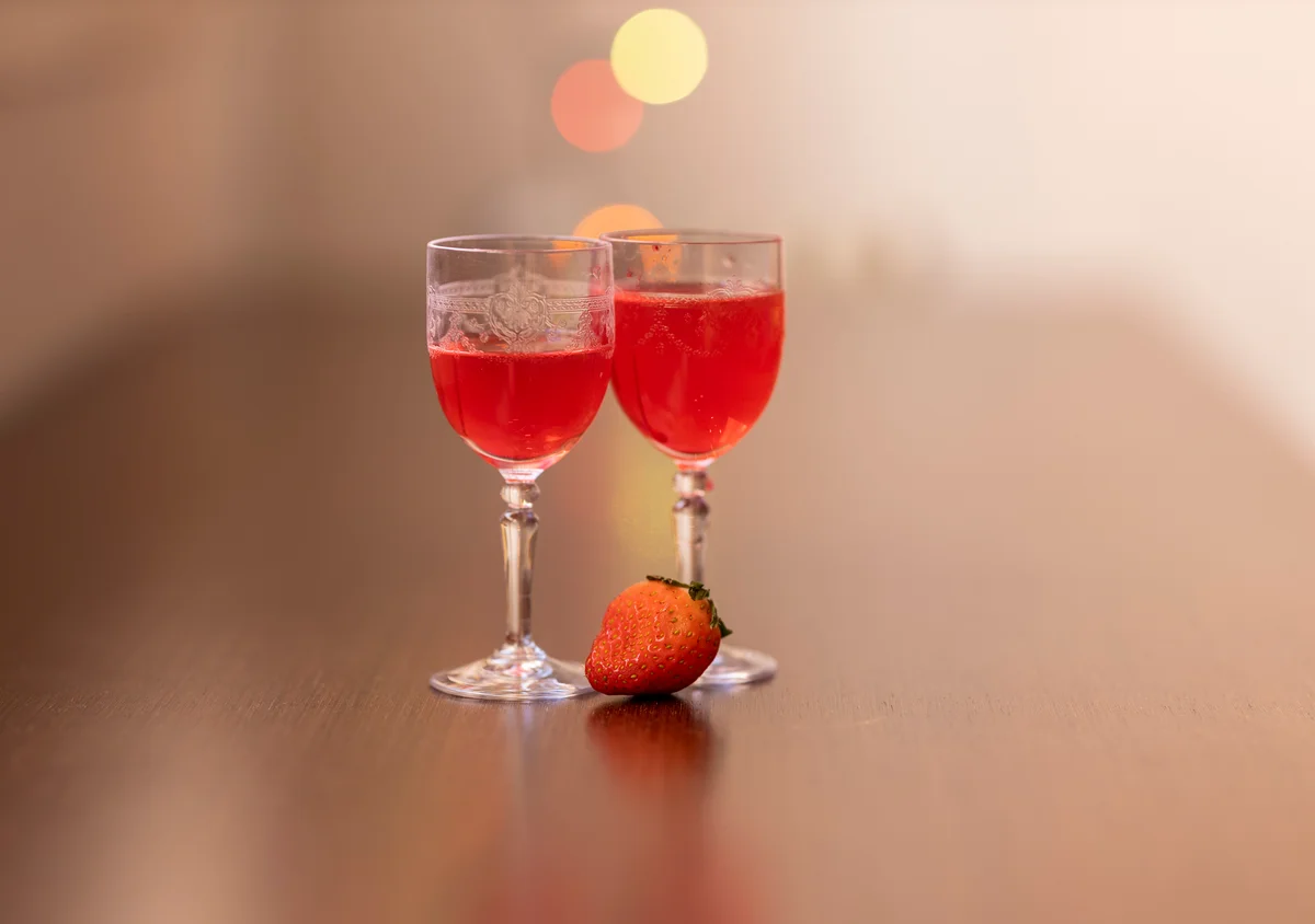 Two small glasses with strawberry drink and a strawberry for garnish on the table