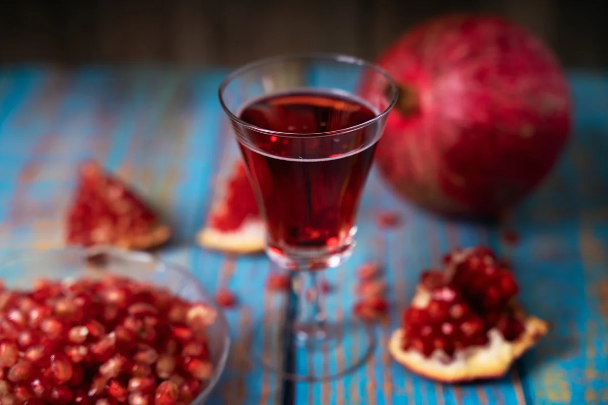 Small glass of pomegranate drink surrounded by pomegranate berries