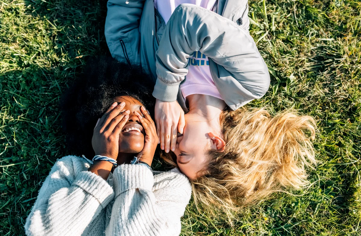 Girls laying grass, one whispering to the other