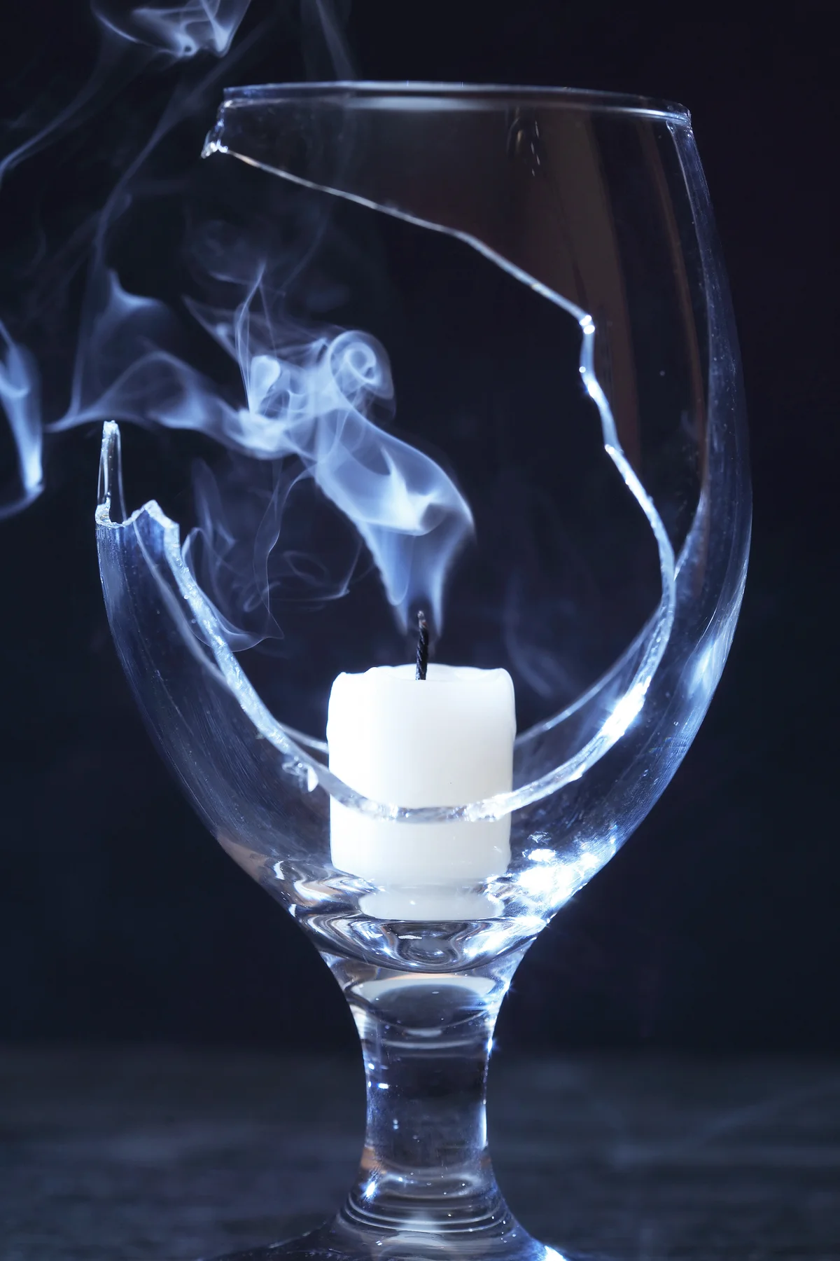 Extinguished candle with smoke inside broken wineglass