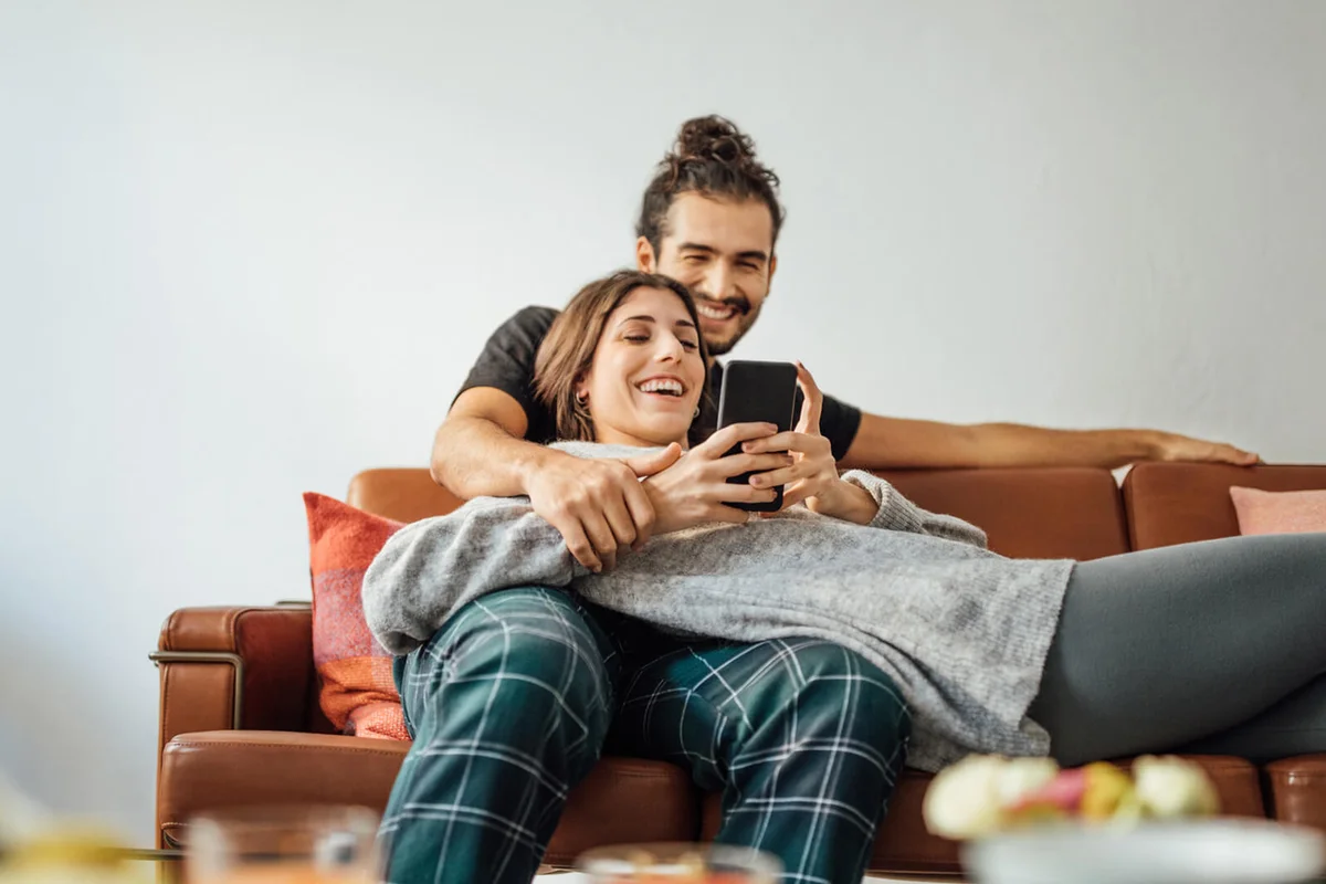 Young couple with smart phone relaxing on sofa