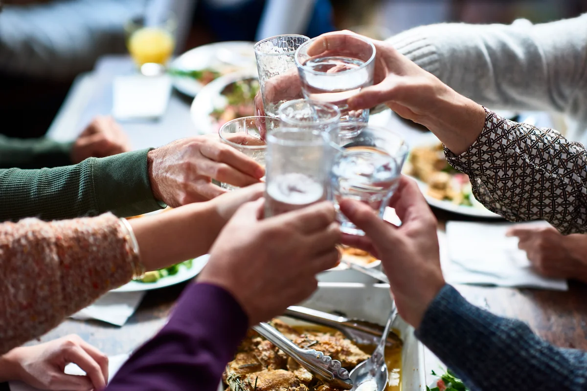 Hands around table cheersing their glasses