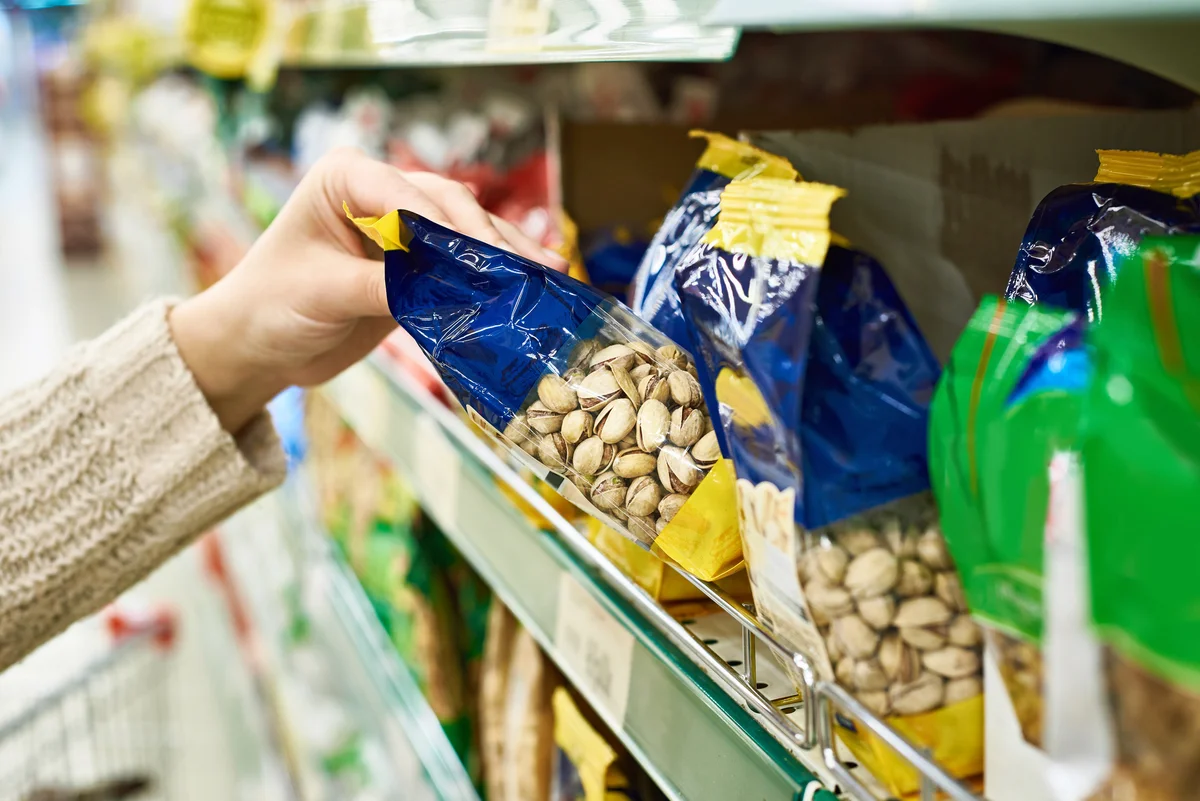 Hand with packing of salted pistachios in store