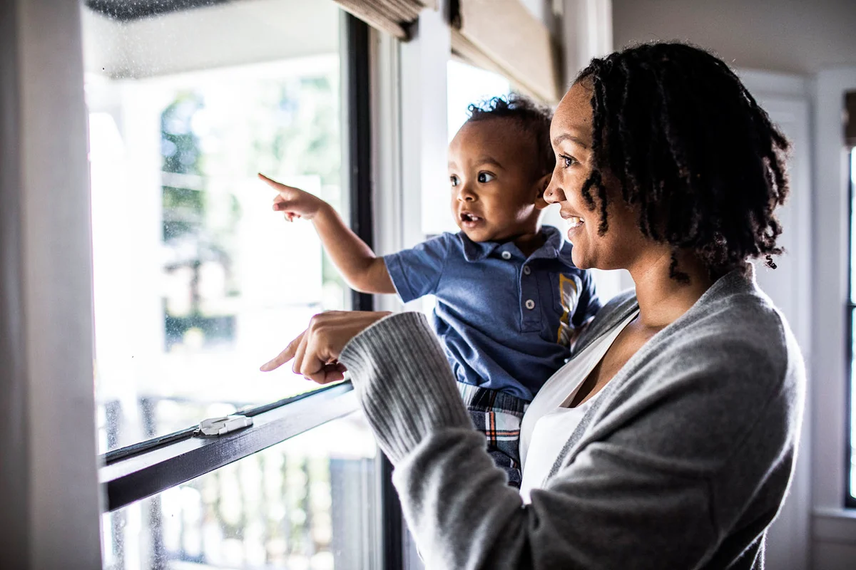 Mother and toddler looking out of home window