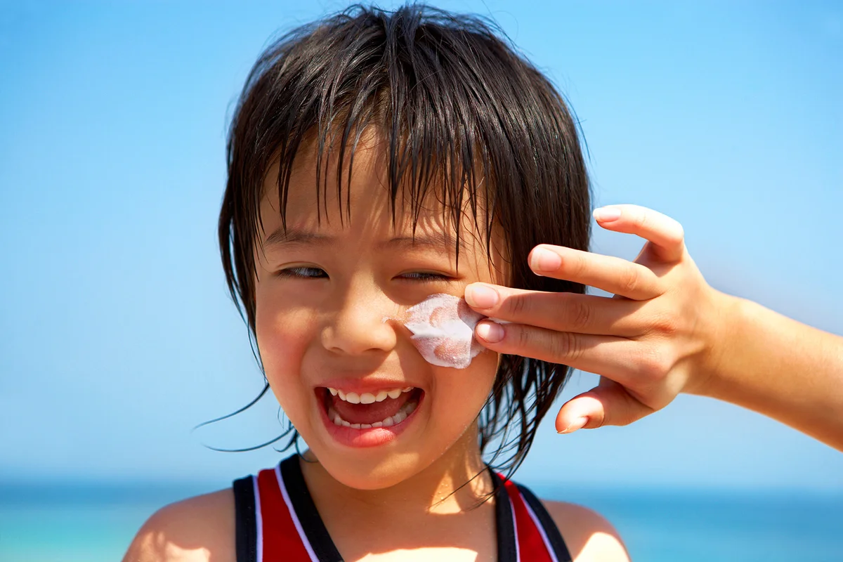 Mother applying sunscreen to kid in the beach