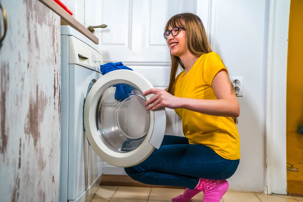 woman using a washing machine to do laundry at home