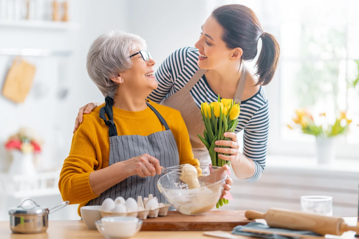 Younger woman giving older woman yellow tulips while they bake