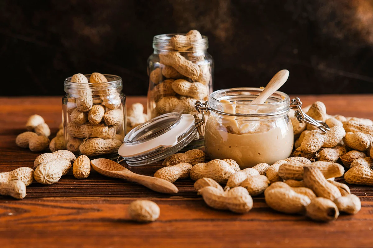 peanuts with butter in jars on wooden table against wall