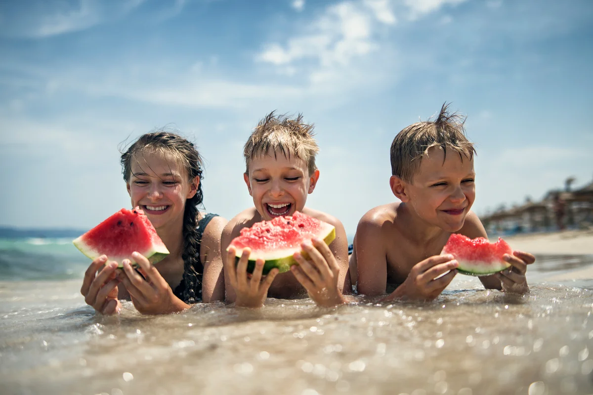 Happy kids eating watermelon on the beach