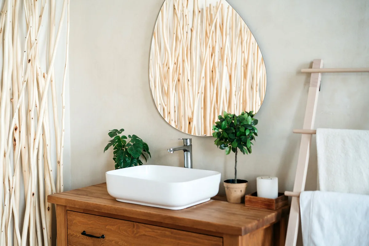 A white sink on a wooden countertop, an oval mirror on the wall